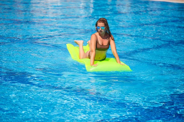 Jeune homme sexy en maillot de bain nage dans la piscine sur un matelas gonflable. Fille en lunettes de soleil dans une piscine bleue en vacances — Photo