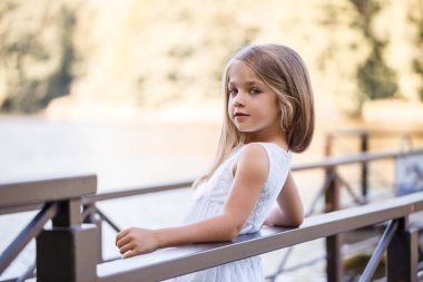 Yazın göl kenarında küçük bir kızın portresi. Nehrin kıyısındaki yazlık elbiseli küçük kız.