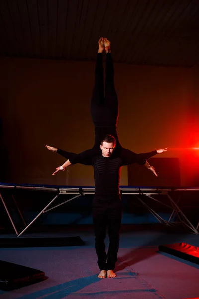 A duo of acrobats performing a doubles trick. A woman in gymnastic overalls and a man in sportswear. Very flexible circus performers.