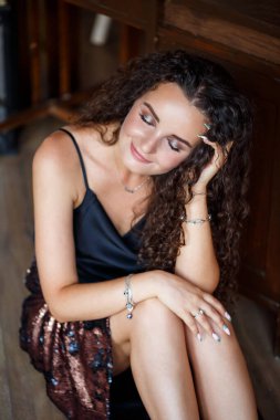 Genç ve çekici bir kadının portresi kıvırcık saçlı, açık tenli, siyah bluzlu ve yüzünde bir gülümsemeyle.