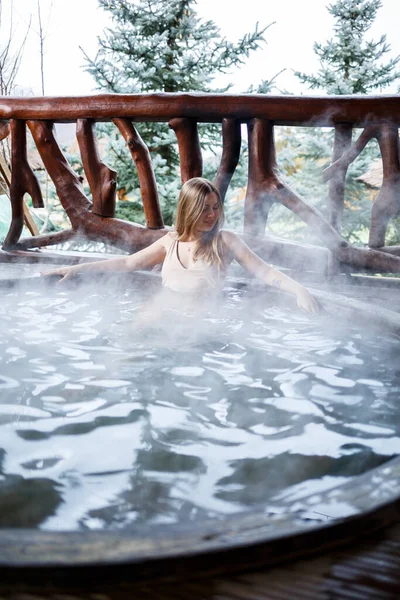 水着姿の美しい女性 テラスでお湯でプールの女の子 スパボディトリートメント 屋外ジャグジー 女の子とジャグジー 開放的な空気の中でリラックスしてください 温泉付きコテージ — ストック写真