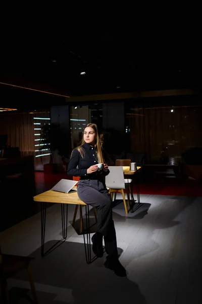 Normal working day of modern woman businessman. Beautiful young woman holding a cup of coffee while sitting at her workplace