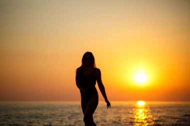 Bir kızın siluetleri denizin arka planında ve batan güneşin altında