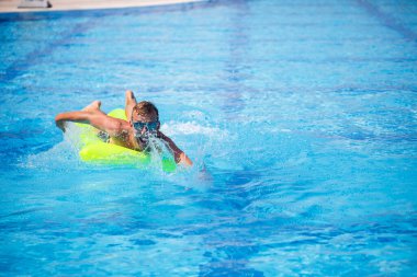 Yakışıklı genç adam mavi havuzda şişme yatakta yüzüyor.