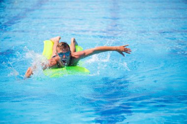 Yakışıklı genç adam mavi havuzda şişme yatakta yüzüyor.