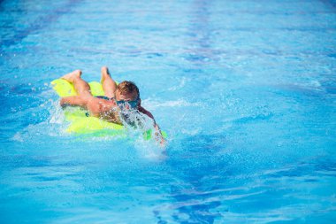 Yakışıklı genç adam mavi havuzda şişme yatakta yüzüyor.