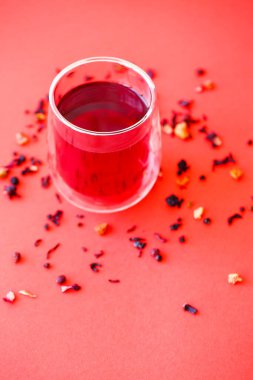 Kırmızı zemin üzerinde çift tabanlı şeffaf bardakta sıcak amber çayı.