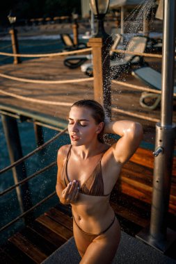 Güzel genç bir kadın açık denizde güneşli bir günde mayoyla rahatlatıcı bir duş alır. Tatildeki kız dinleniyor. Seçici odak