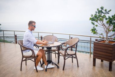 Akdeniz 'e bakan bir dizüstü bilgisayarla havuz kenarında oturan yakışıklı, genç ve başarılı bir iş adamı. Tatilde uzaktan çalışma. Tatil kavramı