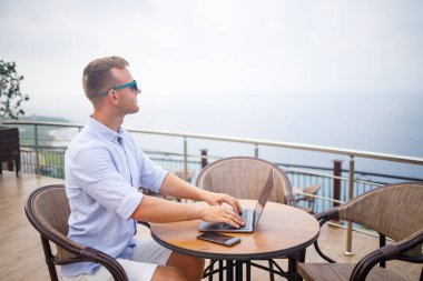 Akdeniz 'e bakan bir dizüstü bilgisayarla havuz kenarında oturan yakışıklı, genç ve başarılı bir iş adamı. Tatilde uzaktan çalışma. Tatil kavramı