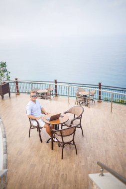 Akdeniz 'e bakan bir dizüstü bilgisayarla havuz kenarında oturan yakışıklı, genç ve başarılı bir iş adamı. Tatilde uzaktan çalışma. Tatil kavramı