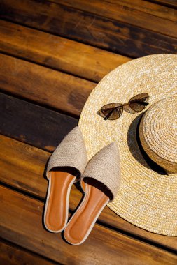 Kadınlar yaz şapkası, güneş gözlükleri ve katır ayakkabıları tahta bir arka planda yatıyor. Bir yazı ya da reklam için yer