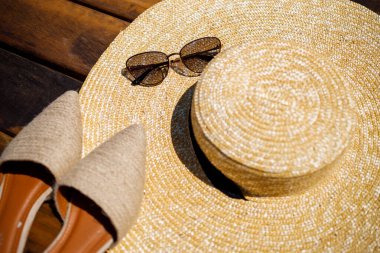 Kadınlar yaz şapkası, güneş gözlükleri ve katır ayakkabıları tahta bir arka planda yatıyor. Bir yazı ya da reklam için yer