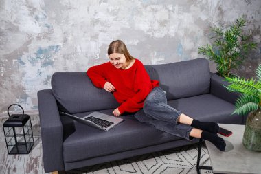 Rahat bir evde rahat bir koltukta oturan ve uzaktan modern bir dizüstü bilgisayarla çalışan serbest çalışan bir kadın internet sitesinde internetten webinar izleyen deneyimli bir kadın. Karantina sırasında evden çalışmak