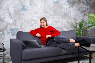 Rahat bir evde rahat bir koltukta oturan ve uzaktan modern bir dizüstü bilgisayarla çalışan serbest çalışan bir kadın internet sitesinde internetten webinar izleyen deneyimli bir kadın. Karantina sırasında evden çalışmak