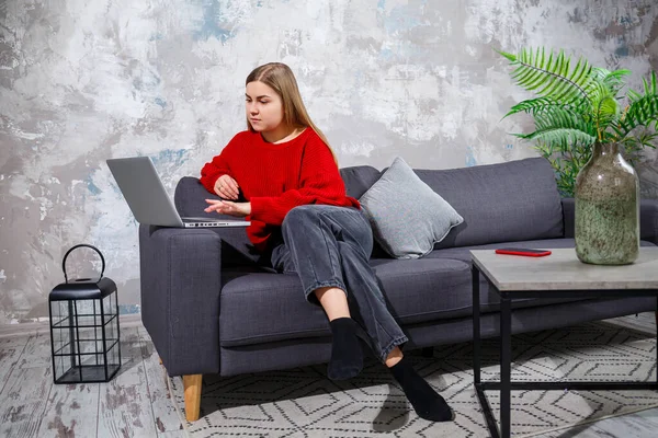 Kanepede oturan genç bir kadın dizüstü bilgisayarın ekranına bakıyor. İnternette bilgisayar üzerinde çalışan motive olmuş, ev tabanlı, serbest çalışan bir bayan öğrenci..