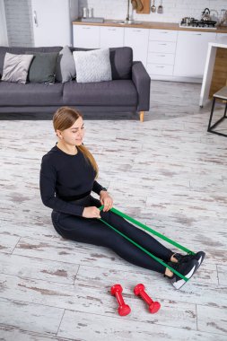 Evde spor yaparken elastik bantla egzersiz yapan gülümseyen genç bir kadın. Sağlıklı yaşam tarzı kavramı. Karantina sırasında evde spor