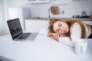 Genç bir kadın mutfakta dizüstü bilgisayarla ders çalışıyor. Evden uzakta çalış.