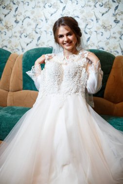 Profesyonel makyajlı bir gelinin yakın plan fotoğrafı. Beyaz önlüklü, duvak takıyor. Kanepede oturup gelinliğe bakmak. Genç bir kadının düğün günü. Fotoğraf, saç stili, güzellik.