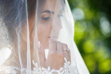 Uzun beyaz bir gelinlik içinde mutlu bir gelinin portresi ve yeşil bir parkta yüzü peçeyle. Genç bir kızın düğün resmi, kadın makyajı ve saç stili. Evlilik kavramı