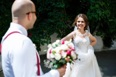 Beyaz gömlekli ve pantolonlu bir damat, beyaz elbiseli ve peçeli güzel bir gelin, düğün günü sokakta poz veriyor ve yürüyor.