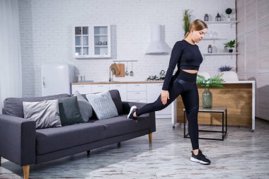 Tozlu, spor ayakkabılı ve bluzlu genç bir kız evde kanepede egzersiz yapıyor. Sağlıklı bir yaşam tarzı. Kadın spor için eve gidiyor..