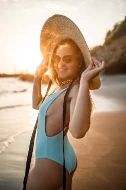 Mayolu genç bir kadın ve gün batımında deniz kıyısında bir şapka. Yaz tatili kavramı. Seçici odak