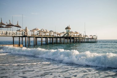 Plaj manzarası ve Akdeniz, güneşli bir günde güzel, berrak deniz suyu. Sıcak bir ülkede dinlenme kavramı. Su üzerinde duran ahşap iskele.
