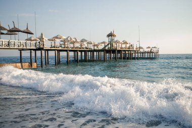 Plaj manzarası ve Akdeniz, güneşli bir günde güzel, berrak deniz suyu. Sıcak bir ülkede dinlenme kavramı. Suyun üzerinde duran ahşap iskele. Seçici odak