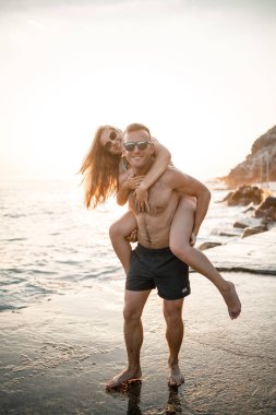 Sevgi dolu bir çift deniz kenarında yürüyor. Akdeniz kıyısında gün batımında genç bir aile. Tatil konsepti. Gün batımında mayolu bir kadın ve deniz kenarında şortlu bir adam. Seçici odak.