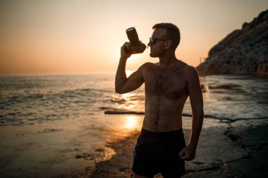 Genç erkek fotoğrafçı gün batımında kıyıda dururken denizin fotoğraflarını çeker. Deniz batımı. Seçici odaklanma. Turist fotoğrafları deniz manzarası