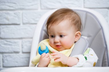 Küçük bir çocuk yüksek bir sandalyeye oturur ve ağdan meyve yer. Bebekleri beslemek için Nibbler