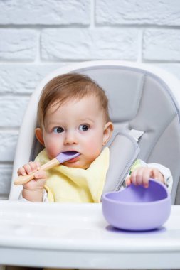 Küçük bir çocuk sandalyeye oturur ve kaşıkla tabaktan yemek yer. Bebekleri beslemek için bebek silikonları