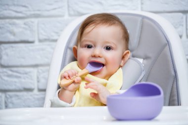 Küçük bir çocuk sandalyeye oturur ve kaşıkla tabaktan yemek yer. Bebekleri beslemek için bebek silikonları