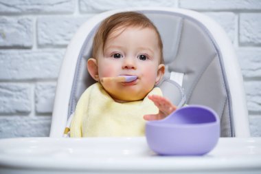 Küçük bir çocuk sandalyeye oturur ve kaşıkla tabaktan yemek yer. Bebekleri beslemek için bebek silikonları