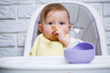 Küçük bir çocuk sandalyeye oturur ve kaşıkla tabaktan yemek yer. Bebekleri beslemek için bebek silikonları