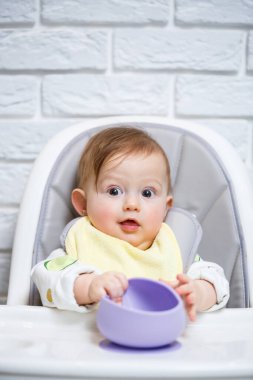 Küçük bir çocuk sandalyeye oturur ve kaşıkla tabaktan yemek yer. Bebekleri beslemek için bebek silikonları