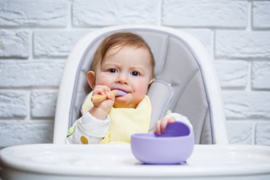 Küçük bir çocuk sandalyeye oturur ve kaşıkla tabaktan yemek yer. Bebekleri beslemek için bebek silikonları
