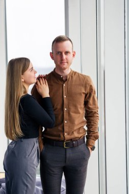 Geniş panoramik pencerelerin önünde aşık şık genç bir çift. Genç bir kadın ve bir adam büyük bir pencerenin yanında duruyor.