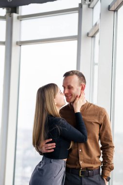 Geniş panoramik pencerelerin önünde aşık şık genç bir çift. Genç bir kadın ve bir adam büyük bir pencerenin yanında duruyor.
