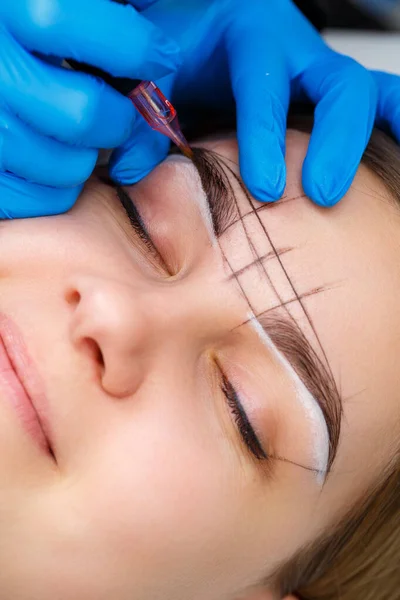 Beautician tattooing a woman\'s eyebrows using special equipment during permanent make-up, close-up.