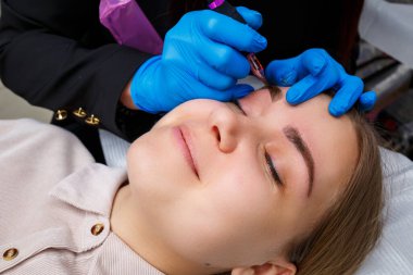 Güzellik salonunda gür kaşları olan güzel bir kadının yüzü. Kaşlar için kalıcı makyaj. Güzellik uzmanı kadınlar için kaş dövmesi yapar. Güzellik prosedürü.