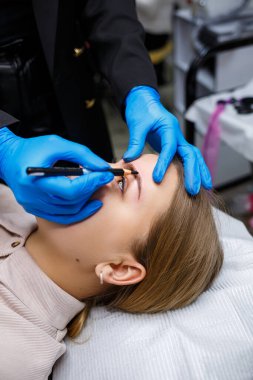 Makyaj sanatçısı, kaş kalemi olan genç bir kızın kaşlarına bir çizim uygular. Profesyonel makyaj ve estetik cilt bakımı.