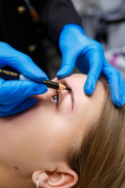 Makyaj sanatçısı, kaş kalemi olan genç bir kızın kaşlarına bir çizim uygular. Profesyonel makyaj ve estetik cilt bakımı.