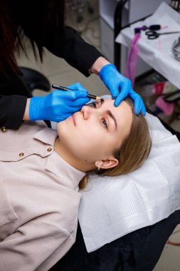 Makyaj sanatçısı, kaş kalemi olan genç bir kızın kaşlarına bir çizim uygular. Profesyonel makyaj ve estetik cilt bakımı.