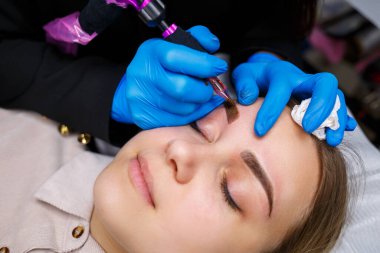 Güzellik salonunda gür kaşları olan güzel bir kadının yüzü. Kaşlar için kalıcı makyaj. Güzellik uzmanı kadınlar için kaş dövmesi yapar. Güzellik prosedürü.