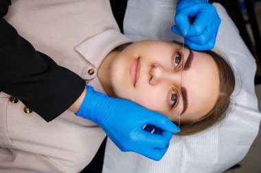 Kaşlarında kalıcı makyaj dövmesi olan bir kadın. Güzellik uzmanı kaşların bir taslağını çiziyor. Profesyonel makyaj ve estetik cilt bakımı.