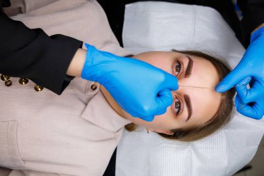 Kaşlarında kalıcı makyaj dövmesi olan bir kadın. Güzellik uzmanı kaşların bir taslağını çiziyor. Profesyonel makyaj ve estetik cilt bakımı.