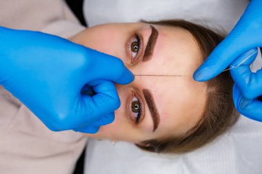 Kaşlarında kalıcı makyaj dövmesi olan bir kadın. Güzellik uzmanı kaşların bir taslağını çiziyor. Profesyonel makyaj ve estetik cilt bakımı.