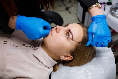 Kaşlarında kalıcı makyaj dövmesi olan bir kadın. Güzellik uzmanı kaşların bir taslağını çiziyor. Profesyonel makyaj ve estetik cilt bakımı.